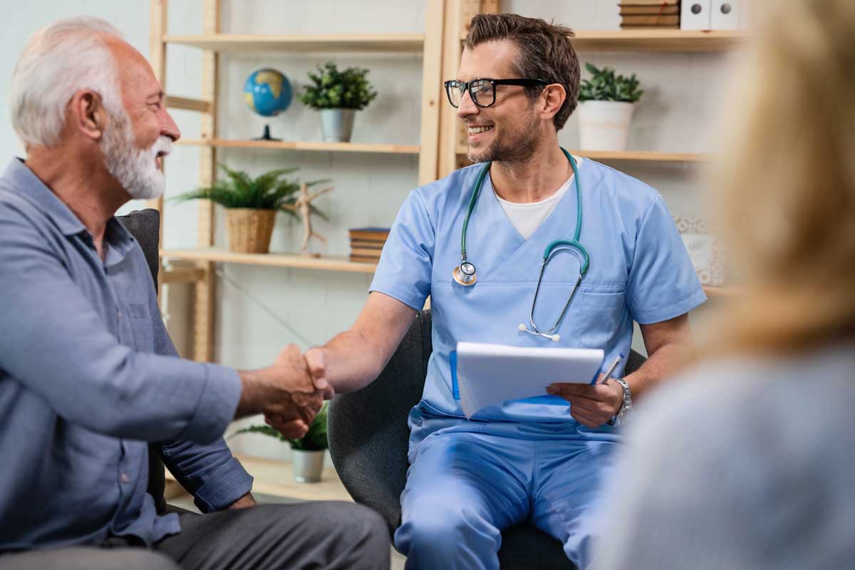 Happy healthcare worker shaking hands with senior man while being in a home visit.